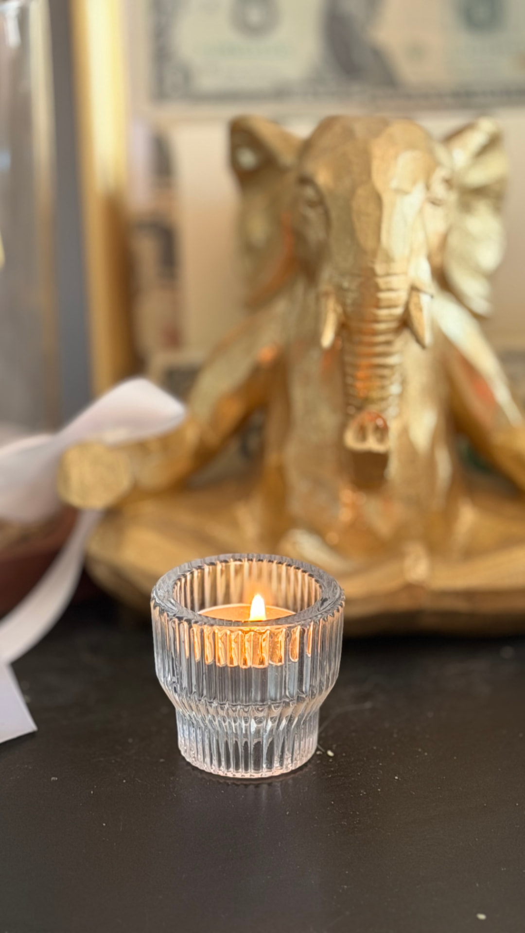A ribbed glass tealight burning in front of a small gold elephant statue